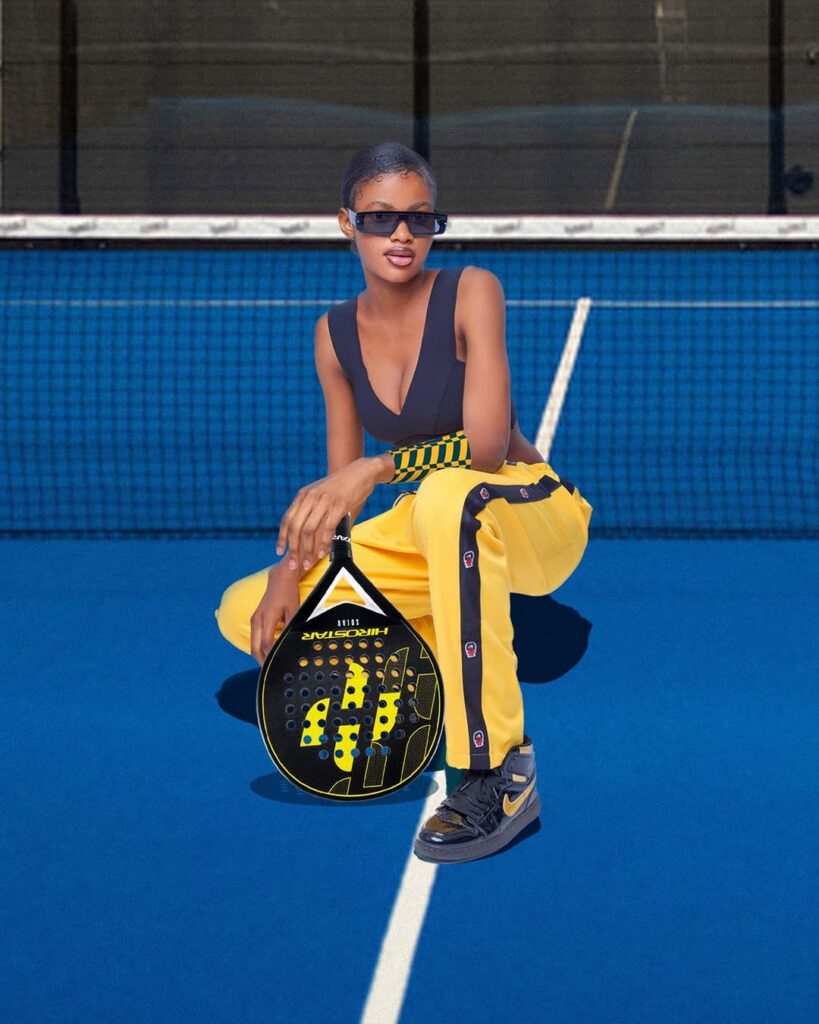 a woman in yellow pants and sunglasses holding a racket